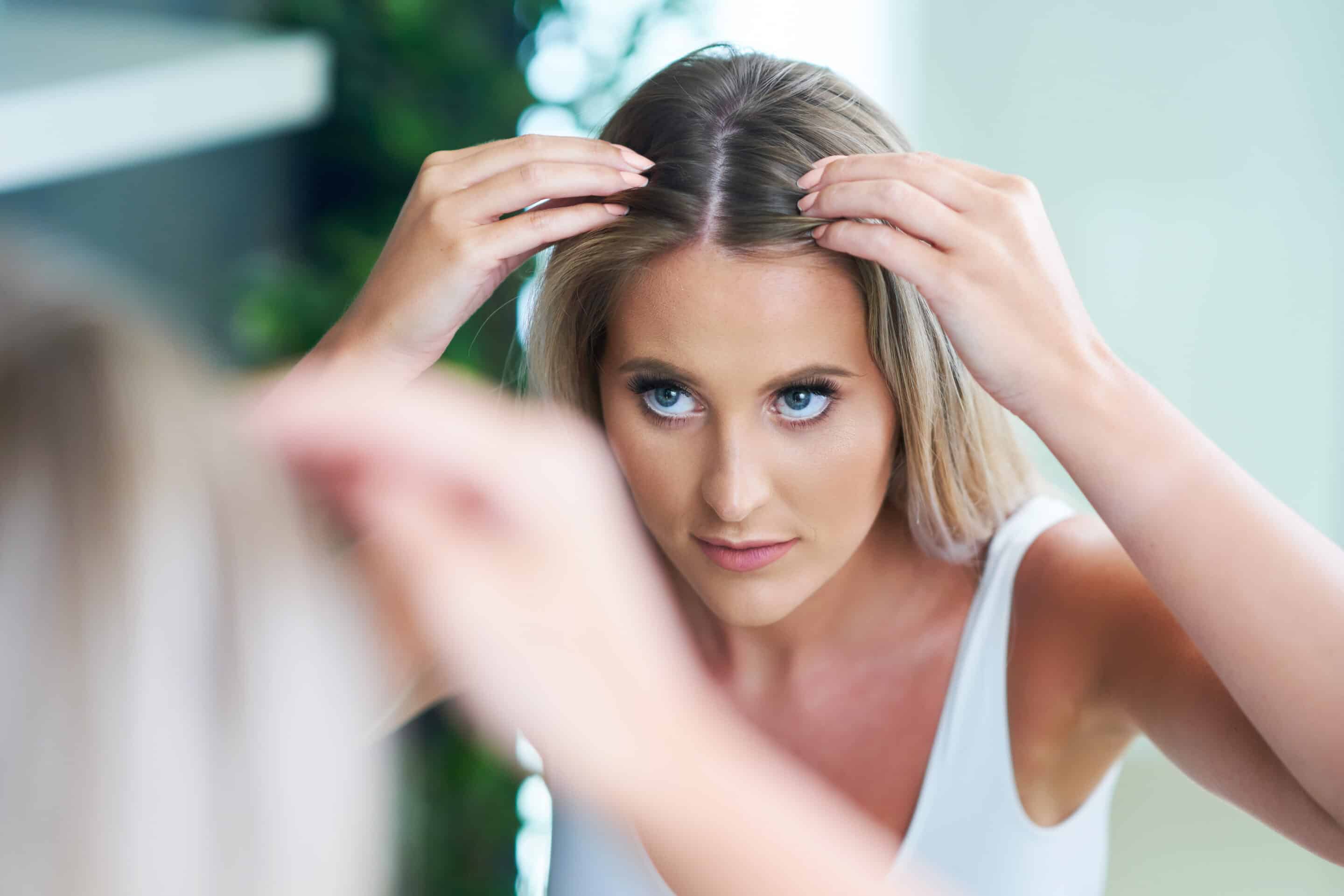 Eine Frau betrachtet Ihren Haarausfall im Spiegel, der durch bestimmte Hormone verursacht wird