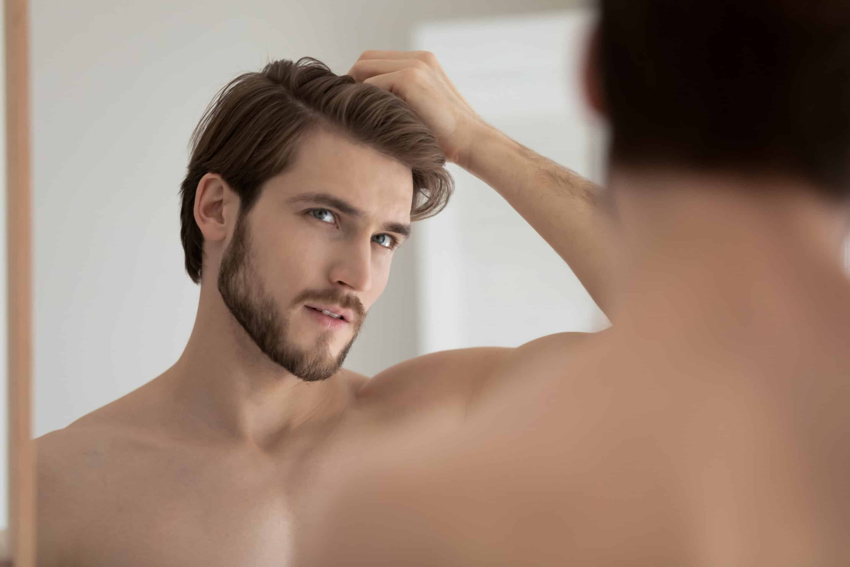 Ein Mann, der durch Corona an Haarausfall litt, betrachtet seine Haare nach einer Haartransplantation im Spiegel